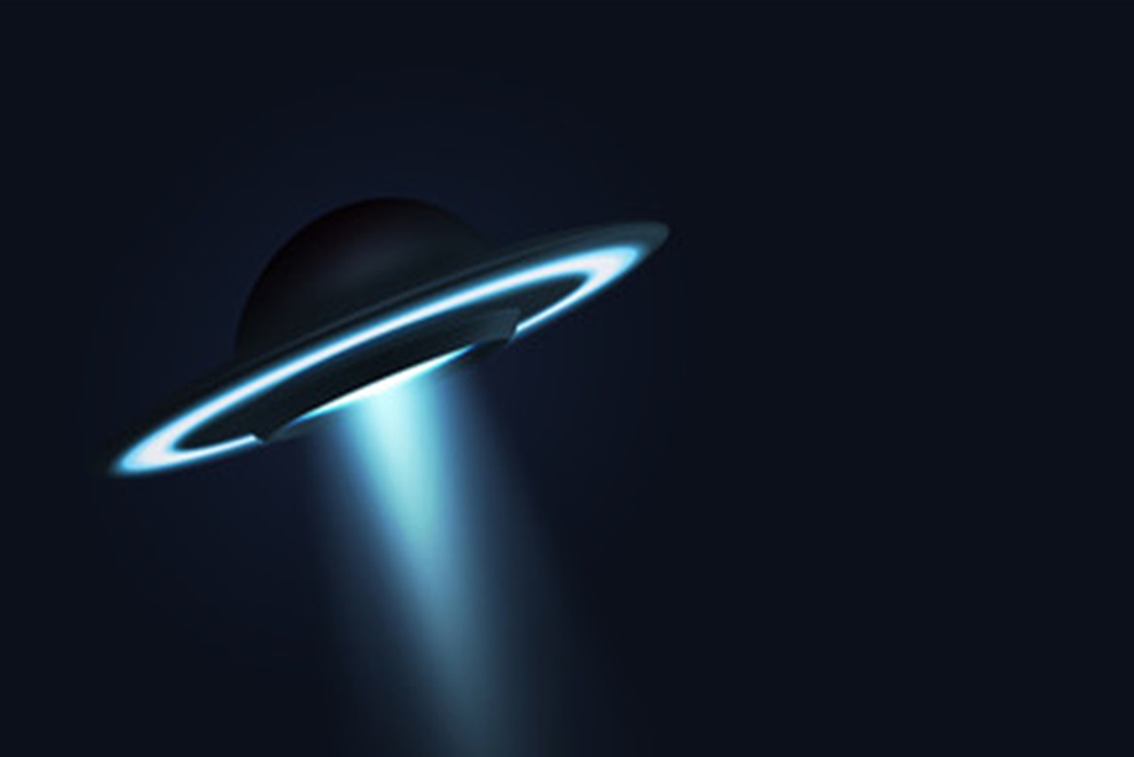 Round spaceship in the night sky with a beam of light shining from the bottom