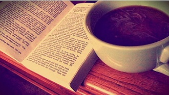 Picture of a cup of coffee beside an open book.