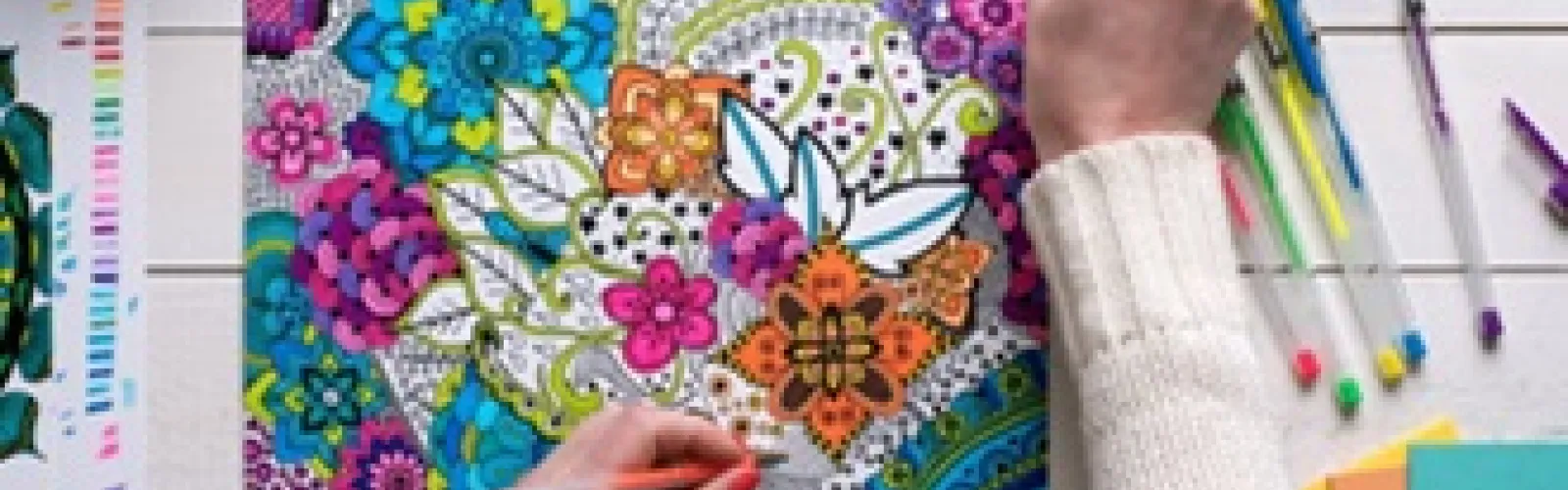 Aerial view of left handed woman coloring a design with gel pens.