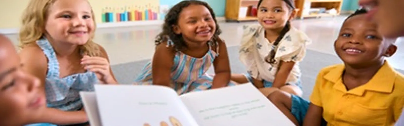 Children sitting in a semicircle around a lady holding open a picture book.