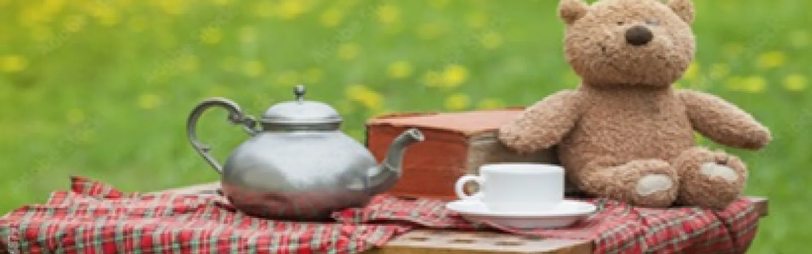A stuffed bear having a picnic with a pod of tea and a cup on a saucer.