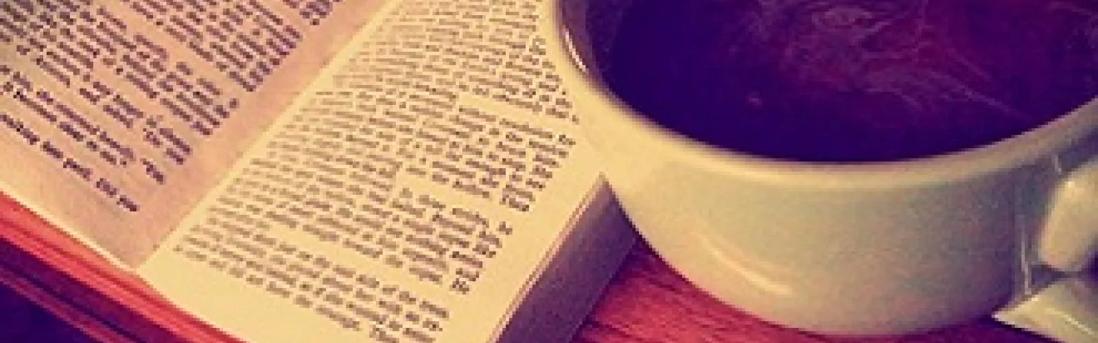 Picture of a cup of coffee beside an open book.